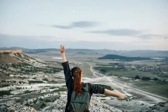 Уверенная в себе женщина обнимает ночное небо, стоя на вершине горы