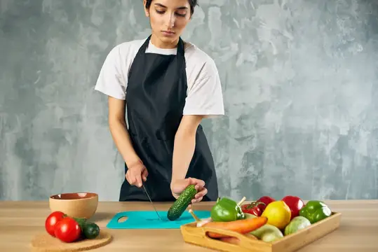 Молодая женщина в фартуке режет огурец на кухне