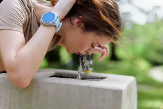 Девушка пьёт воду из фонтанчика в парке