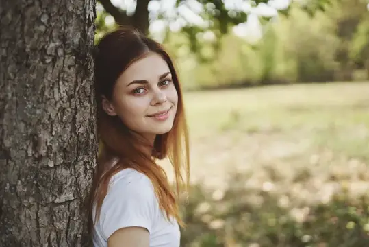 Жизнерадостная женщина стоит рядом с деревом на природе, солнце, свобода, путешествие