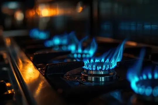На изображении запечатлено голубое пламя на газовой плите в современной кухне, подчёркивающее красоту приготовления пищи