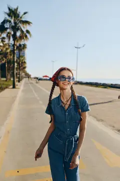 Улыбающаяся девушка с косичками и в очках гуляет по набережной с пальмами