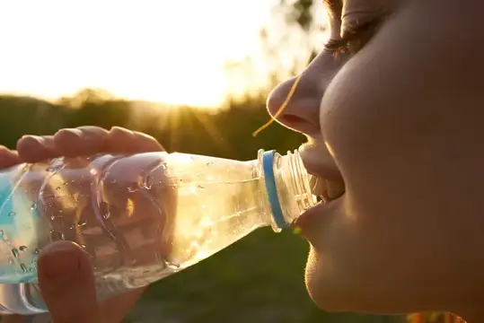 Девушка пьёт воду из бутылки на закате