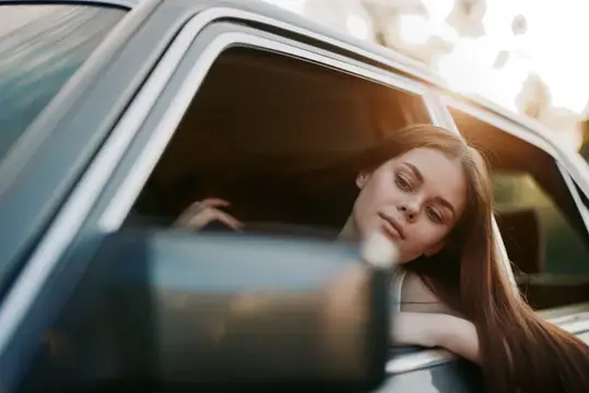 Рыжеволосая девушка высунулась из окна автомобиля на закате