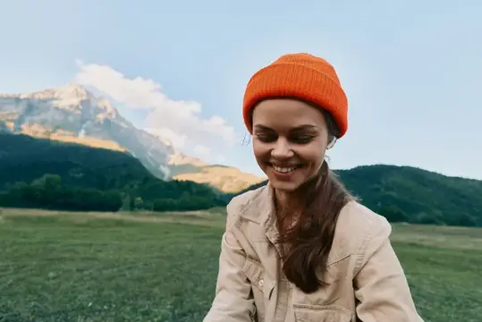 Улыбающаяся девушка в оранжевой шапке на фоне гор