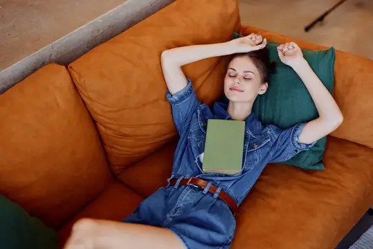 Молодая женщина отдыхает с книгой на оранжевом диване