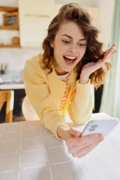 Удивлённая девушка с телефоном за столом на кухне