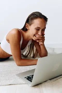 Женщина работает из дома за ноутбуком, фрилансер, работающий на дому, занимается онлайн-трейдингом, лежит на полу и улыбается, обнажая зубы