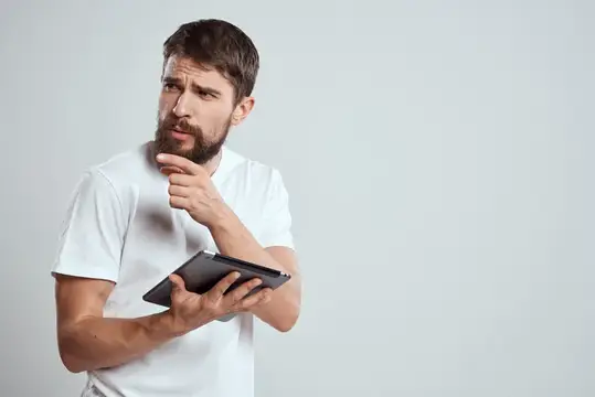 Задумчивый бородатый мужчина с планшетом в белой футболке