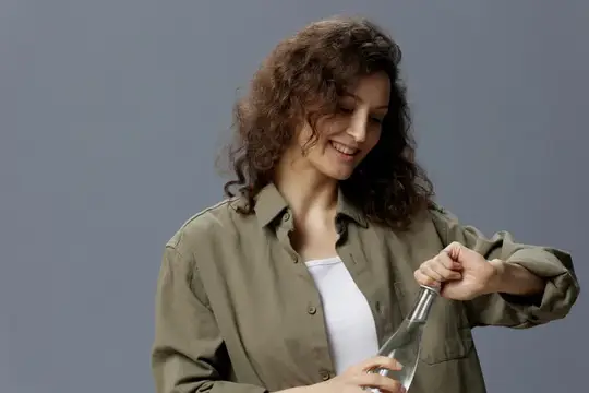 Кудрявая девушка в рубашке откручивает крышку стеклянной бутылки
