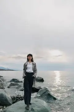 Молодая женщина в плаще стоит на камнях у моря в пасмурный день