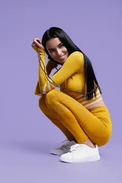 Улыбающаяся брюнетка в жёлтом спортивном костюме сидит на корточках