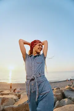 Улыбающаяся девушка в джинсовом комбинезоне и красной бандане на закатном пляже
