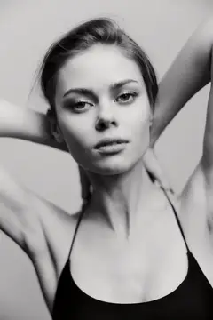 Молодая женщина с распущенными волосами в чёрном топе на светлом фоне