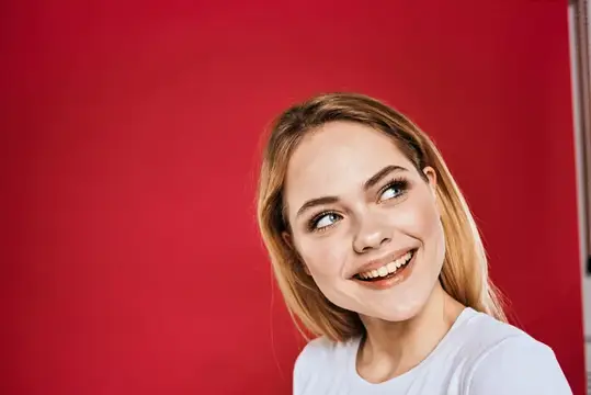 Улыбающаяся блондинка смотрит в сторону на красном фоне