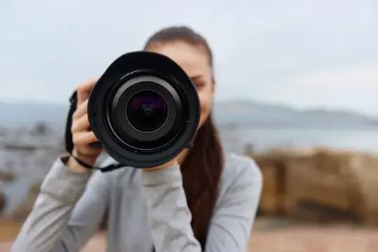 Молодая женщина с энтузиазмом держит фотоаппарат, готовая запечатлеть красивые пейзажи, подчеркивая свою страсть к фотографии на природе в безмятежном естественном окружении