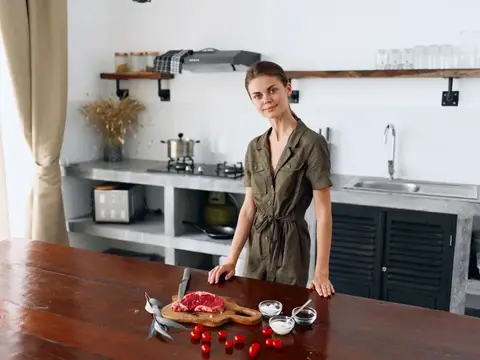 Молодая женщина в кухне у стола с мясом и помидорами