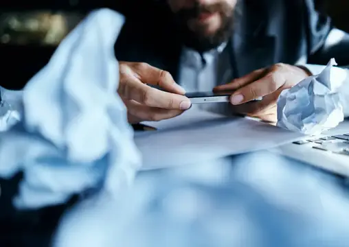 Мужчина в костюме листает смартфон среди скомканных бумаг