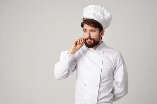 Задумчивый бородатый повар в белом колпаке на сером фоне