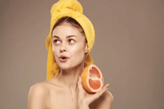 Симпатичная женщина с обнажёнными плечами держит в руке грейпфрут