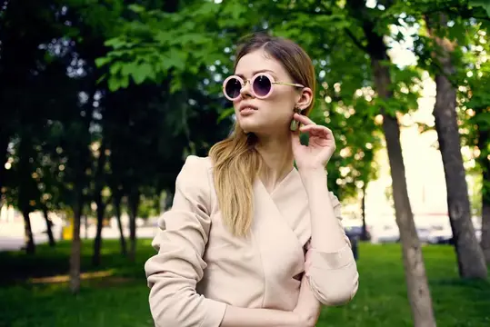Молодая женщина в круглых солнцезащитных очках гуляет по летнему парку