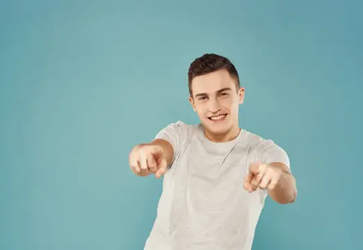 Улыбающийся парень в белой футболке указывает пальцами на камеру