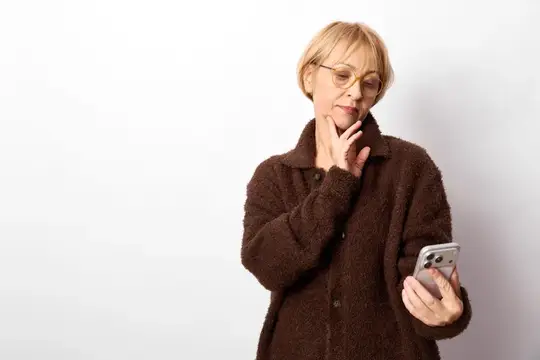 Задумчивая блондинка в очках смотрит в смартфон на светлом фоне