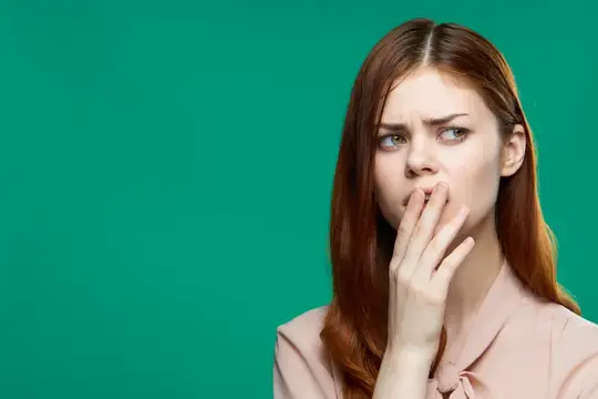 Рыжеволосая девушка прикрывает рот рукой на зелёном фоне