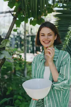 Улыбающаяся темноволосая девушка с миской ягод в оранжерее
