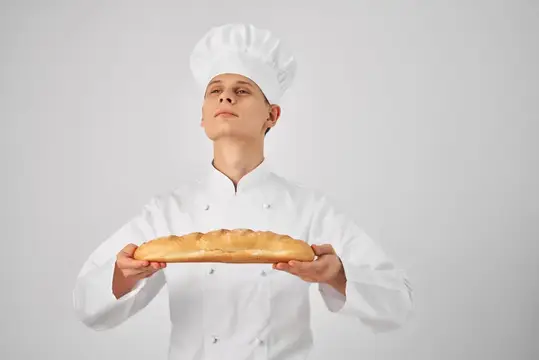 Мужчина в поварской форме держит буханку хлеба, готовя еду
