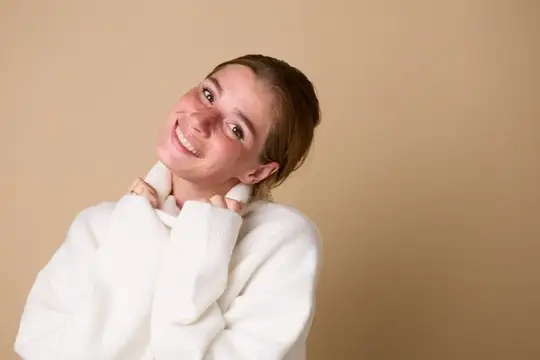 Улыбающаяся молодая женщина в белом свитере на бежевом фоне