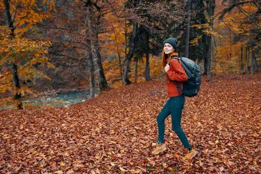 Улыбающаяся девушка с рюкзаком идёт по осеннему лесу