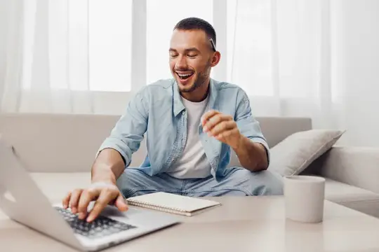 На этом изображении улыбающийся мужчина работает за ноутбуком, что отражает суть мягкой маскулинности и размытия границ между работой и личной жизнью, подчеркивая современную домашнюю экономику и…
