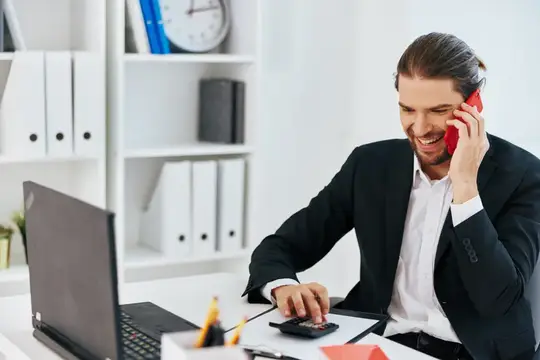 Улыбающийся мужчина в костюме говорит по красному телефону в офисе