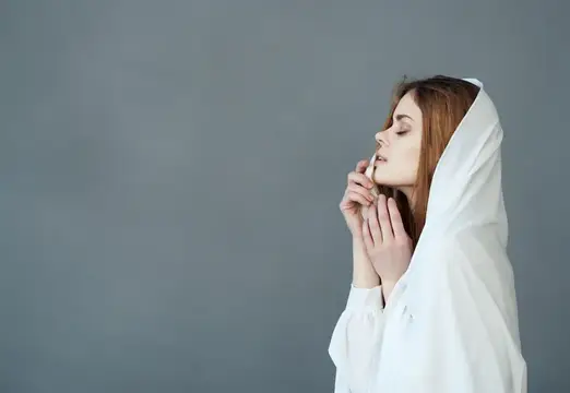 Молодая женщина с закрытыми глазами молится, укрыв голову белой тканью