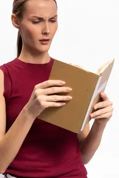 Молодая женщина с недоумением читает книгу в бордовой футболке