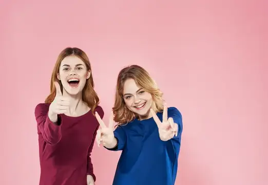Две красивые женщины в элегантном стиле общаются, ведут активный образ жизни и веселятся на розовом фоне
