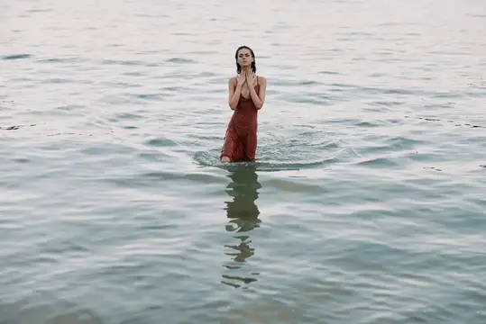 Молодая женщина в бордовом платье стоит по колено в воде