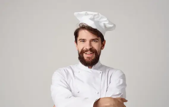 Улыбающийся бородатый повар в белом колпаке на сером фоне