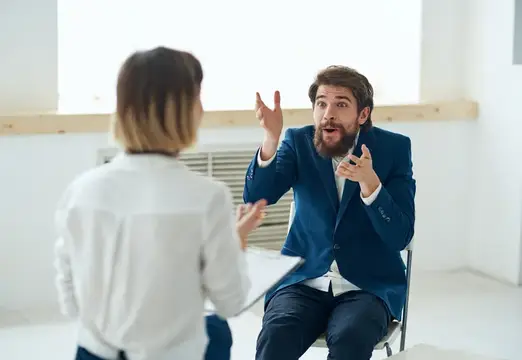 Бородатый мужчина в синем пиджаке эмоционально жестикулирует на встрече с коллегой