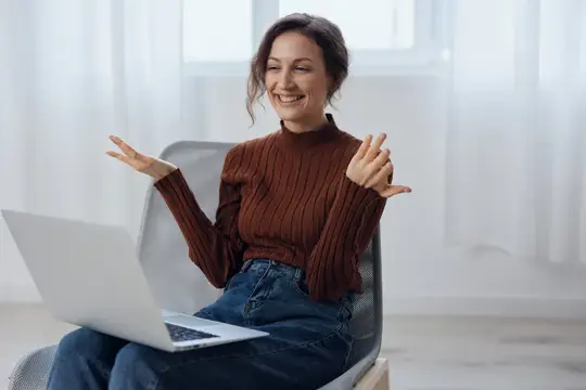 Шокированная, удивленная, счастливая кудрявая великолепная женщина разговаривает с другом по видеоконференции, рассказывает о последних классных новостях, держит ноутбук, поднимает руку и активно…