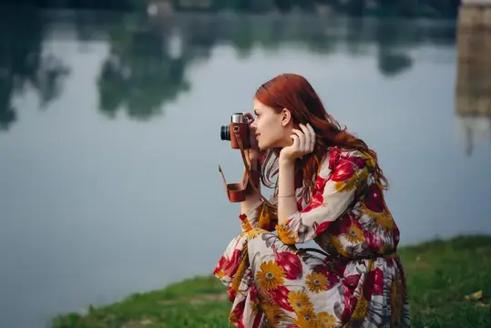 Рыжеволосая девушка с пленочным фотоаппаратом у озера