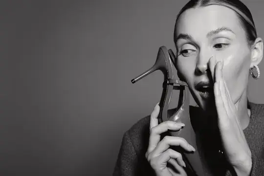 Удивлённая женщина с туфлей на каблуке у лица