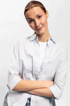 Молодая женщина со скрещёнными руками в светлой рубашке на белом фоне