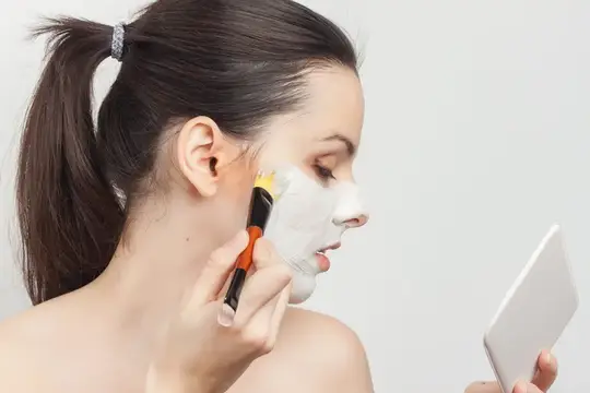 Молодая женщина наносит маску для лица перед смартфоном