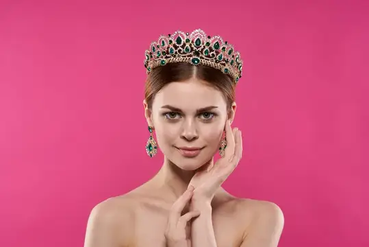 Молодая женщина в роскошной короне с изумрудами на розовом фоне
