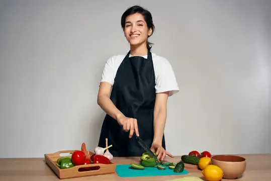 Улыбающаяся девушка в фартуке режет овощи на кухне