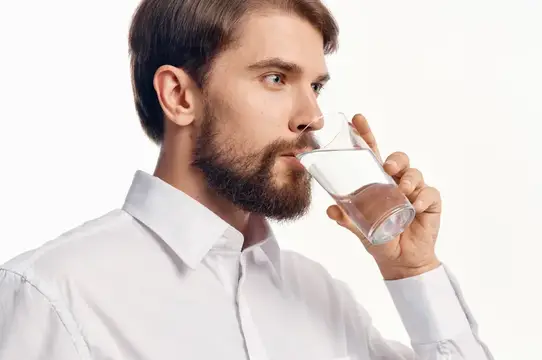 Бородатый мужчина в белой рубашке пьёт воду из стакана