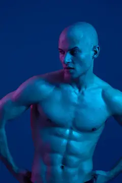 Лысый мускулистый мужчина позирует в синем свете