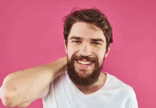 Улыбающийся бородатый мужчина в белой футболке на розовом фоне